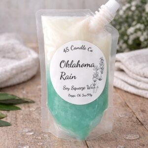 Plastic pouch with a spout that is capped to the right of the bag. Bag is filled with aqua and white wax. The melt bag sits on a wood table with water drops and green leaeves placed around the table top. White babys breath flowers is in the background.