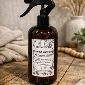 One plastic spray bottle is sitting on a wood table with a rustic indoor background design. The spray bottle has a spray nozzle. The bottle has a brown string wrapped around the top with a bow. The lable has product information consisting of company name, product name (All Purpose Cleaner) , scent name, directions, wight, place made, and warning label.