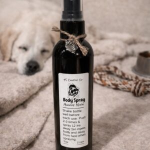 a black misting spray bottle with a clear cap, a string tied around the top of the bottle with a silver paw print attached. The bottle is 4oz in sixe, it has a label with 4S Candle co printed on it, a picture of an english bulldog, the product name: Body Spray, the name Maggie Moon and directions of how to use the product. The bottle sits on a tan rug with a partical picture of a rope, a dog bowl, and a dog sleeping in the background.