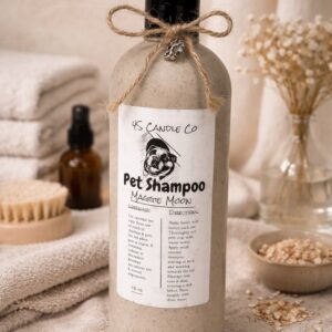 A 16oz tan bottle stis ontop of a tan towl. The bottle has a black cap and a string tied in a bow is attached around the top of the bottle with a silver paw print charm. A white label centers the bottle with the 4S Candel CO name printed on the top, a picture of an english bulldog, the product name of Pet Shampoo and Maggie Moon, Directions and a warneing lable are also on the lable. THe background consists of stacked tan twols, flowers in a vase, a bowl and a brush.